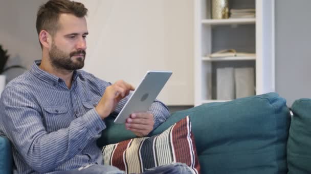 Mann surft auf Tablet-PC im Internet und sitzt auf Couch — Stockvideo