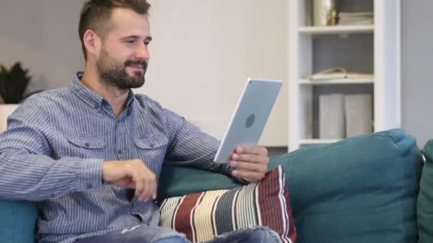 Онлайн видео чат на планшете от человека, сидящего на диване — стоковое видео