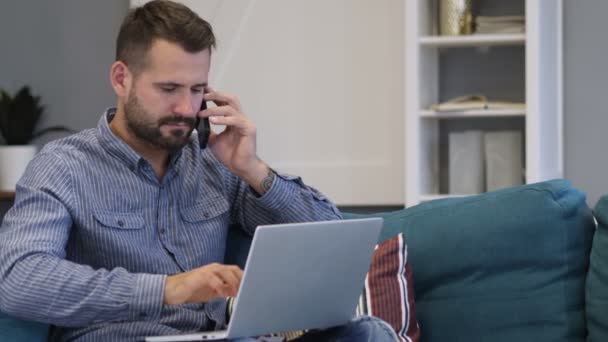 Hombre hablando por teléfono y trabajando en el ordenador portátil — Vídeos de Stock