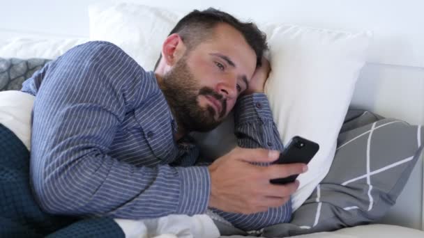 Mann benutzt Smartphone, während er auf der Seite im Bett liegt — Stockvideo