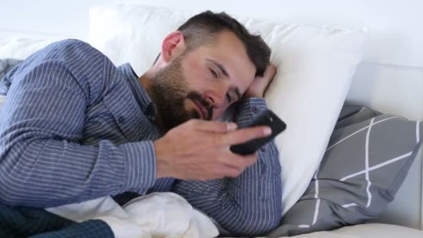 Человек разговаривает по телефону, лежа на кровати — стоковое видео
