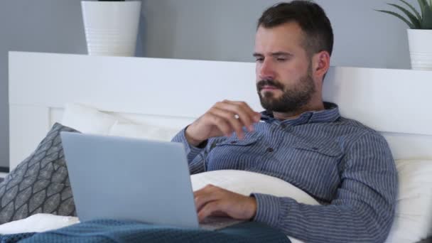 Σκεπτικός ο άνθρωπος σκέφτεται και εργάζονται για το Laptop στο κρεβάτι — Αρχείο Βίντεο