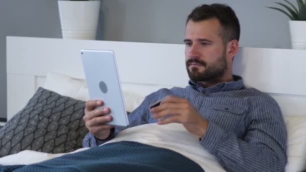 Інтернет-магазини на планшеті втомленого чоловіка в ліжку — стокове відео