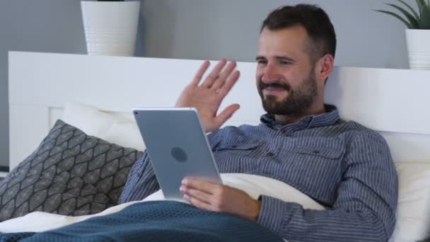 Chat de vídeo en línea en la tableta por el hombre cansado en la cama — Vídeo de stock