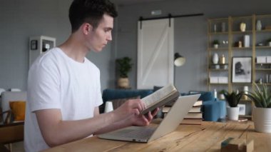 Genç adam okuma kitabı ve çalışma üstünde Laptop