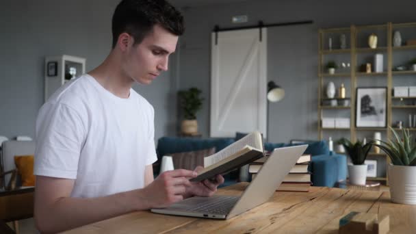 Молодий чоловік читає книгу сидячи на столі — стокове відео