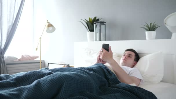 Ο άνθρωπος χρησιμοποιώντας Smartphone ενώ ξαπλωμένος στο κρεβάτι — Αρχείο Βίντεο
