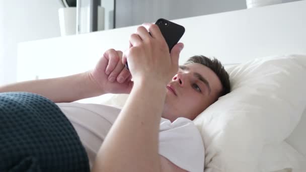 Primer plano del hombre usando Smartphone mientras está acostado en la cama — Vídeo de stock