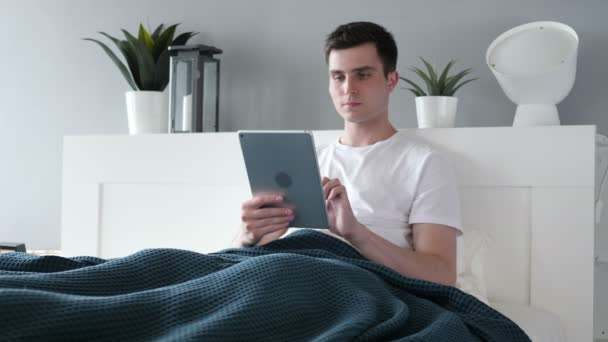 Людина використовує планшет лежачи в ліжку — стокове відео