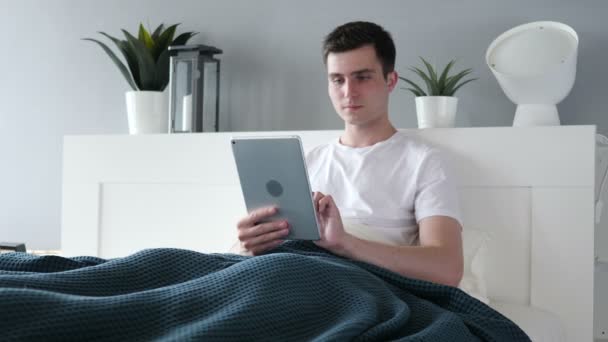 Podekscytowany, wygrywając człowieka za pomocą tabletu w łóżku — Wideo stockowe