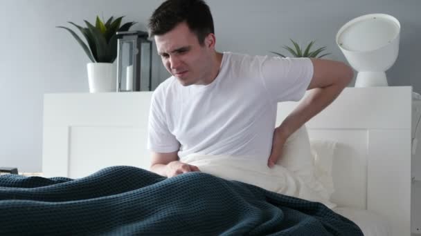 Mann mit Rückenschmerzen sitzt im Bett — Stockvideo