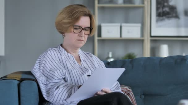 Vieille femme âgée écrivant sur des documents tout en étant assise sur le canapé, paperasserie — Video