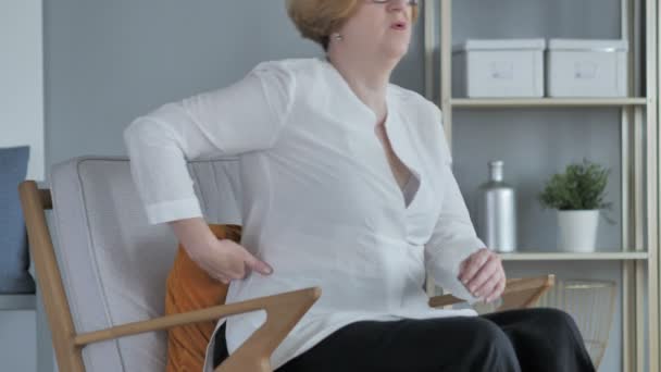 Работающая пожилая женщина с болями в спине сидит на диване — стоковое видео