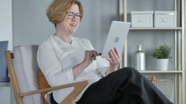 Онлайн видео чат на планшете от пожилой женщины, сидящей на диване — стоковое видео
