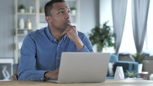 Pensive jonge Afrikaanse man denken en werken op laptop — Stockvideo