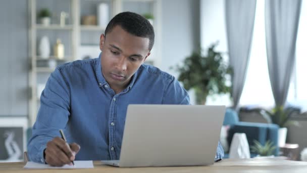 Joven africano escribiendo sobre documentos en el cargo — Vídeos de Stock