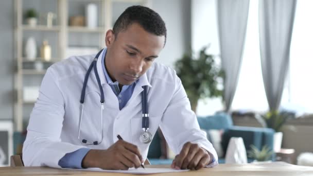 Афроамериканский врач пишет медицинский отчет о пациенте, бумажная работа — стоковое видео