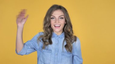 Genç kız üzerinde sarı arka plan izole hoş geldiniz için el sallayarak