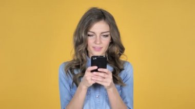 Genç kız üzerinde sarı arka plan izole Smartphone tarama