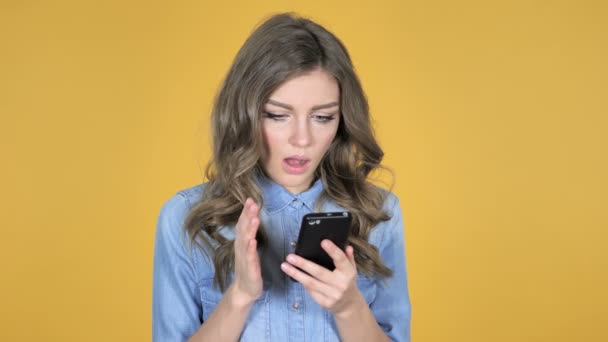 黄色の背景にスマート フォンの分離を使用している間ショックで若い女の子 — ストック動画