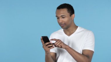 Genç adam African heyecanlı başarı kullanarak Smartphone izole mavi arka plan üzerinde süre için