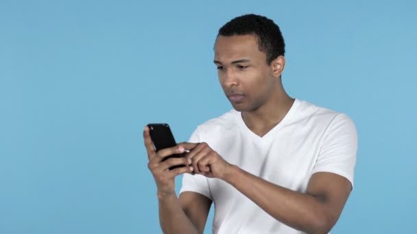 Afrikai Fiatalember Reagál Veszteség Használ Smartphone Elszigetelt Kék Háttér — Stock videók