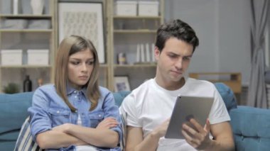 Man Using Tablet while Angry Grilfriend Sitting Aside on Couch