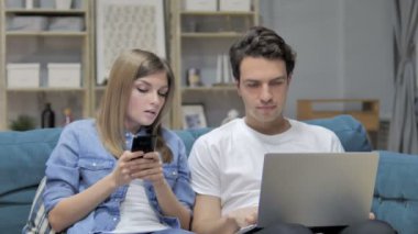 Genç çift konuşurken Smartphone kullanarak ve dizüstü evde