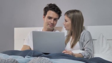 mutlu genç bir çift yatakta dizüstü kullanarak