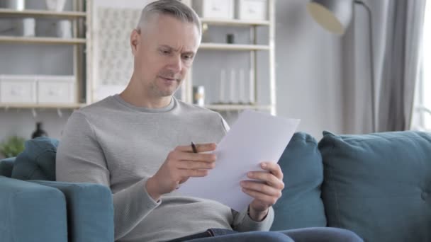 Mann Mit Grauen Haaren Liest Dokumente Während Auf Dem Sofa — Stockvideo