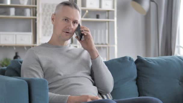 ソファに座りながら電話で話している灰色の髪男 — ストック動画