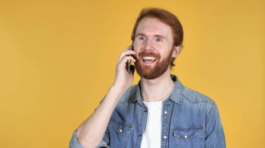 Kızıl saçlı adam sarı arka plan üzerinde izole Smartphone cep telefonu ile konuşmak