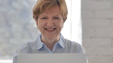 Kameraya bakarak gülümseyen yaşlı kadın