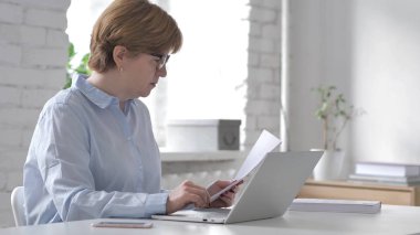 Yaşlı kadının işyerinde, evrak işlerini yapması yazarak