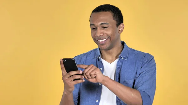 年轻的非洲男子浏览智能手机隔离在黄色背景 — 图库照片