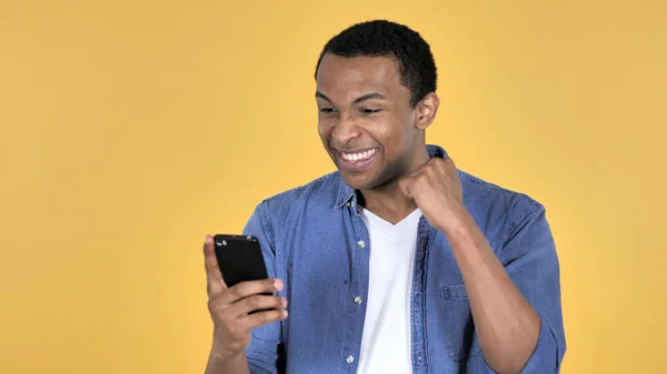 年轻的非洲男人兴奋的成功 而使用智能手机隔离在黄色背景 — 图库照片