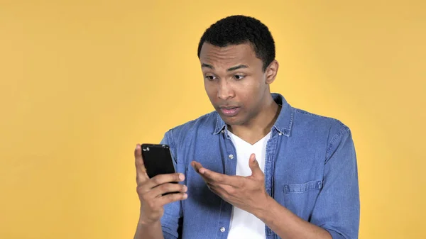 非洲青年在使用黄色背景隔离的智能手机时受到冲击 — 图库照片