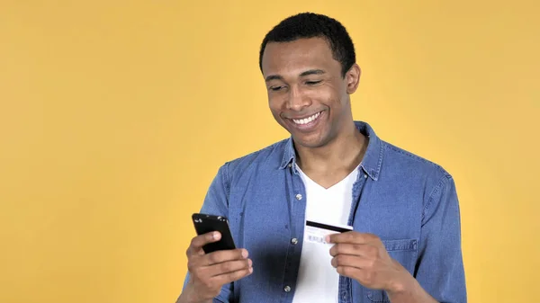 黄色背景隔离的非洲青年在智能手机上网上购物 — 图库照片