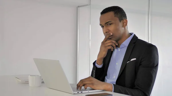 Pensive African Businessman Thinking and Working on Laptop