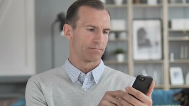 Чоловік середнього віку шокований результатами на телефоні — стокове відео