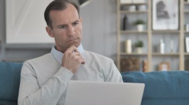 Orta yaşlı adam düşünme ve laptop üzerinde çalışma kanepede otururken