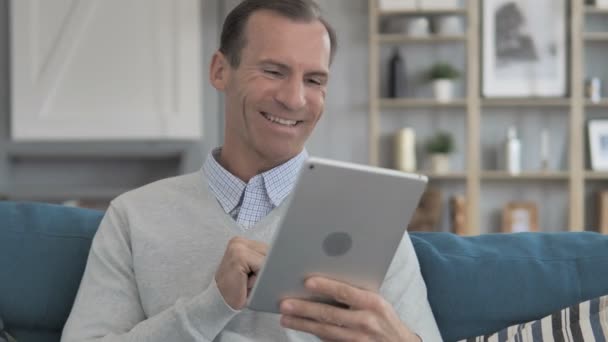 Online Video Chat op Tablet door midden leeftijd Man zit op de Bank — Stockvideo