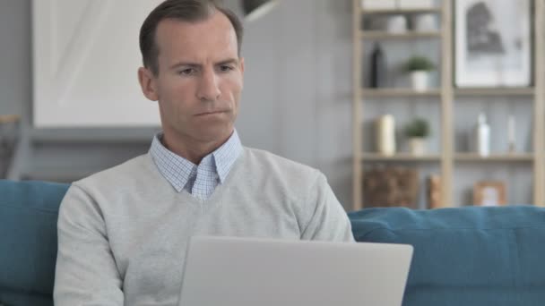 Muž středního věku s bolestmi hlavy práce na přenosném počítači při sezení na gauči — Stock video