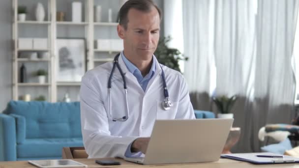 Ανώτερος γιατρός δακτυλογραφεί σε φορητό υπολογιστή στην κλινική, αποστολή ηλεκτρονικού ταχυδρομείου — Αρχείο Βίντεο