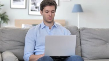 Yakışıklı genç adam düşünme ve laptop üzerinde çalışan kanepede otururken