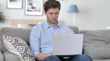 Kanepede otururken yakışıklı genç adam laptop üzerinde çalışıyor