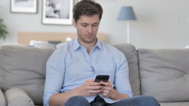 Kanepe üzerinde rahatlatıcı iken Smartphone kullanarak genç adam