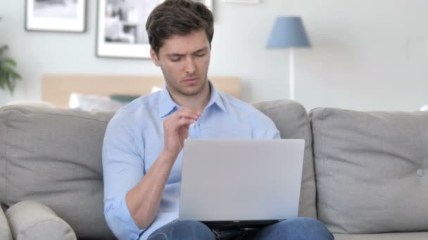 Schöner junger Mann mit Kopfschmerzen bei der Arbeit am Laptop, während er auf der Couch sitzt — Stockvideo