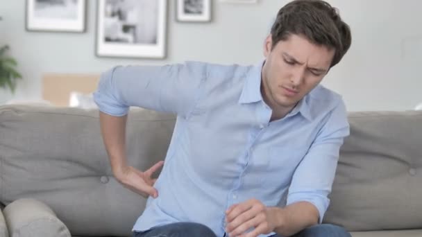 Hombre joven guapo con dolor de espalda vertebral sentado en el sofá — Vídeos de Stock