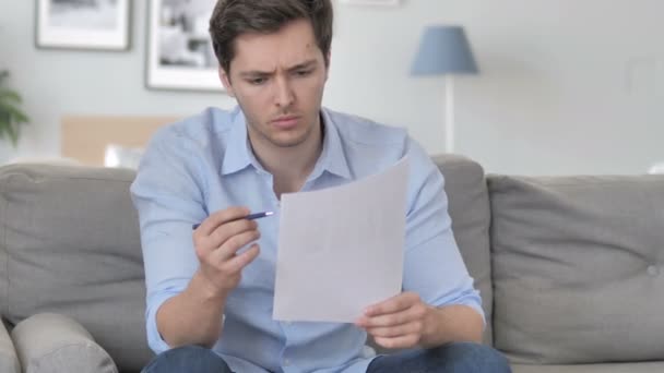 Knappe jonge man het lezen van documenten terwijl zittend op de Bank — Stockvideo